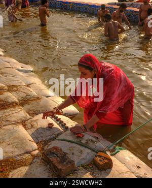 Während der Maha Kumbh Mela in Prayagraj spielt eine Frau im roten Sari Puja im Triveni Sangam, dem heiligen Zusammenfluss von Ganges, Yamuna und Saraswati. Stockfoto