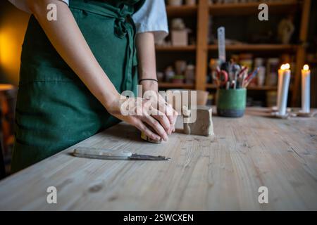 Handwerkerhände kneten Ton für die Herstellung von Naturkeramik auf dem Tisch in der Werkstatt. Kleine Unternehmen Stockfoto