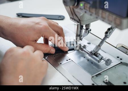 Hände führen den Stoff unter die Nadel einer industriellen Nähmaschine in einem hellen professionellen Arbeitsplatz Stockfoto