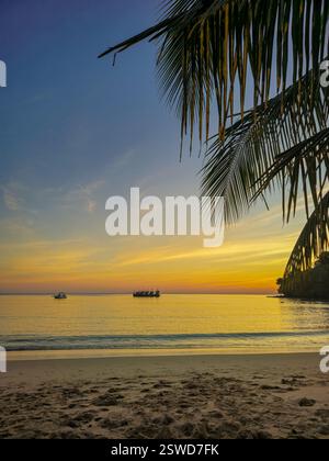 Lebendiger Sonnenuntergang über dem ruhigen Koh Kood Strand in Thailand mit Silhouettenbooten Stockfoto