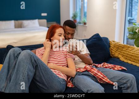Junge, vielseitige Paare, die sich zu Hause mit dem Mobiltelefon ausruhen Stockfoto