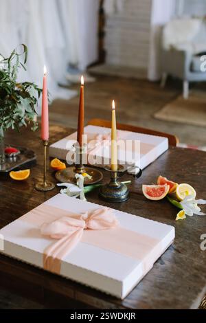 Elegante Geschenkboxen und beleuchtete Kerzen zieren einen Holztisch und unterstreichen das warme Ambiente für ein festliches Treffen. Stockfoto