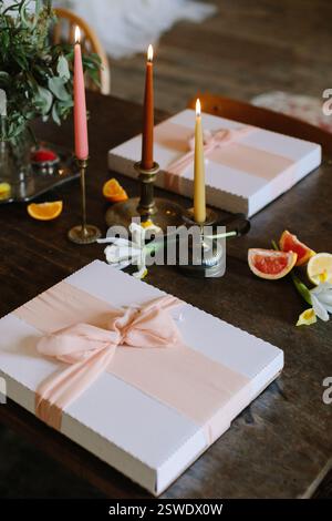 Elegante Geschenke mit Bändern neben zündeten Kerzen und verstreuten Früchten schaffen eine warme Atmosphäre. Stockfoto