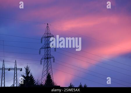 Strommasten, die sich vor einem leuchtenden Sonnenuntergangshimmel abzeichnen Stockfoto