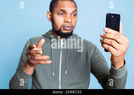 Junge zwanglose, entspannte Person, die mit Freunden im Videonetzwerk diskutiert, mit Freunden vor blauem Hintergrund tratscht, afroamerikanischer Erwachsener positiv und freundlich ist. Stockfoto