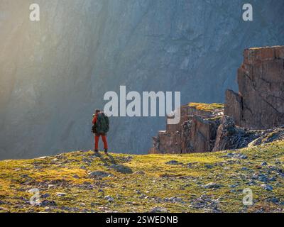 Fotograf mit großem Rucksack macht Fotos von einer wunderschönen Berglandschaft am Rande einer Klippe. Stockfoto