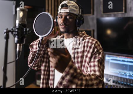 Junger Mann nimmt Gesang für neues Hitalbum in professionellen Musikstudios auf, mit Popfilter und Kopfhörern Stockfoto