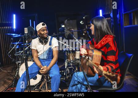 Zwei Musiker arbeiten an einem Song zusammen, spielen Akustikgitarre und nehmen Gesang in einem professionellen Musikstudio auf Stockfoto