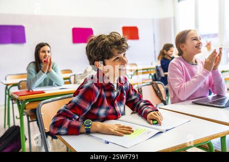 Grundschüler sitzen an Schreibtischen und hören dem Lehrer aufmerksam zu, während sie sich Notizen machen während eines spannenden Unterrichtsunterrichts Stockfoto