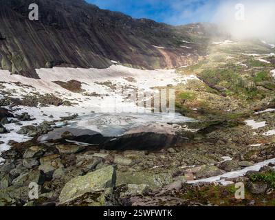 Fantastischer Blick auf den nebeligen Black Lake mit riesigen Steinen am Ufer im Ergaki Nature Park. Sommerlandschaft mit kristallklarem blauen See mit Stockfoto