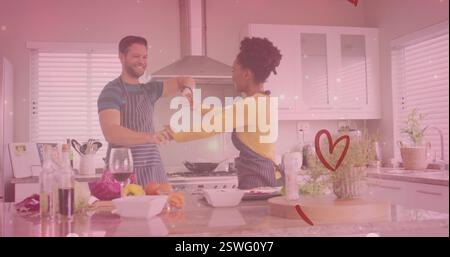Bild von Herzen über verschiedenartiges Paar, das zu Hause in der Küche tanzt Stockfoto