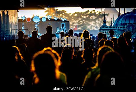 Silhouettenmenschen, die auf ein helles Licht zugehen, mit künstlerischen Wandgemälden im Hintergrund. Die Szene fängt eine lebendige Atmosphäre während der Sonnen ein Stockfoto