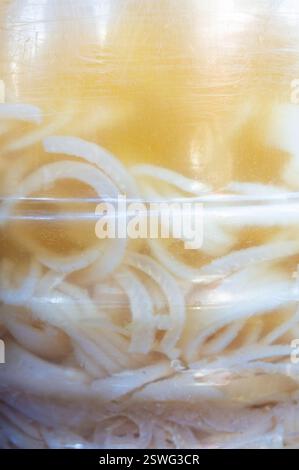 Nahaufnahme traditioneller mexikanischer eingelegter Schweinefleischscheiben in Essig, gelagert in einem großen transparenten Gefäß. Perfekt für mexikanische Street Food-Kultur, Stockfoto