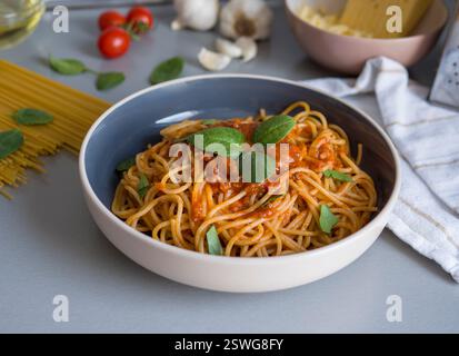 Balanesi-Pasta mit reichhaltiger Tomatensauce, garniert mit frischem Basilikum, eingebettet in eine elegante Keramikschale mit rohen Zutaten und Küchenutensilien Stockfoto