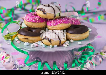 Donuts, Berliner, Krapfen mit Streamer und Konfetti. Buntes Bild von Karneval, Geburtstag und fasching, rosa Hintergrund Stockfoto