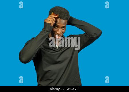 Ein lächelnder junger Athlet kämmt sein kurzes Afro-Haar mit einem Kamm Stockfoto