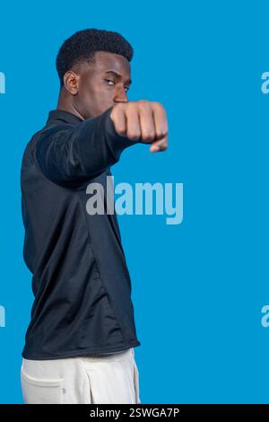 Ernsthafter junger Athlet, der Boxen übt und einen Schlag auf blauem Hintergrund wirft Stockfoto