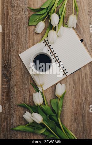 Eine Tasse Kaffee, ein offenes Buch und ein Blumenstrauß auf der Holzplatte. Flache Ausführung mit Draufsicht. Kopierbereich. Stockfoto