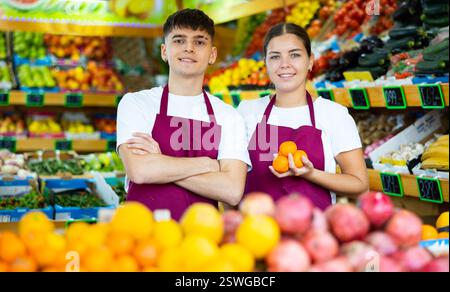 Positiv lächelnde Verkäuferin und Verkäufer in der Schürze, die frisches Obst im Geschäft anbietet Stockfoto
