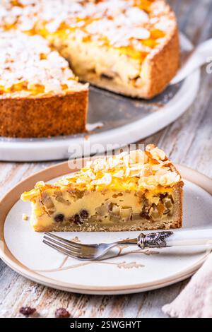 Ein Stück hausgemachter Apfelkuchen mit gerösteten Mandeln auf weißem Holzhintergrund, ganzer Kuchen im Hintergrund, vertikal Stockfoto
