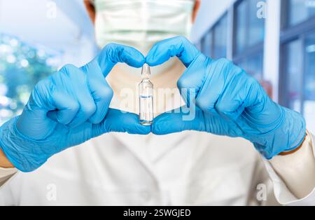 Ein medizinisches Fachpersonal in blauen Handschuhen präsentiert ein klares steriles Fläschchen, während es eine Maske trägt, in einer medizinischen Einrichtung, die sich auf die Patientenversorgung konzentriert. Stockfoto