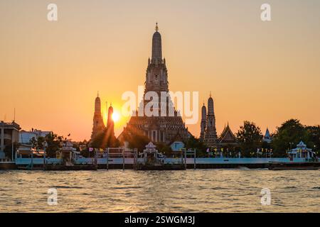 Sonnenuntergang über dem Wat Arun mit goldenen Tönen auf dem Chao Phraya Fluss in Bangkok, Thailand Stockfoto