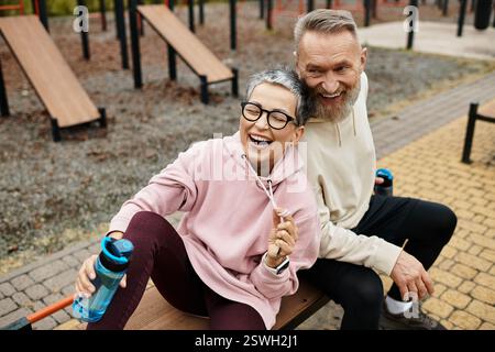 Ein reifes Paar sitzt glücklich auf einer Bank, lacht und teilt freudige Momente nach dem Training. Stockfoto