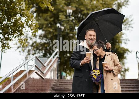Ein liebevolles Paar teilt einen freudigen Moment unter einem Sonnenschirm und schlürft Kaffee, während es von der Natur umgeben ist. Stockfoto