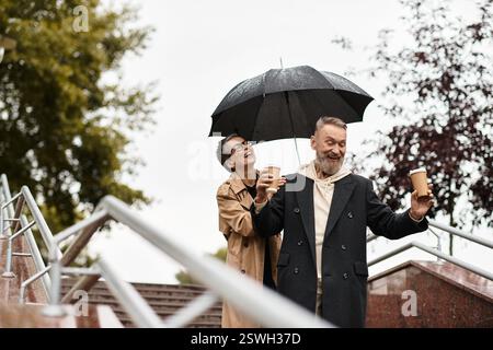 Ein Paar lacht unter einem Regenschirm und schlürft Kaffee, während er im Regen läuft. Stockfoto