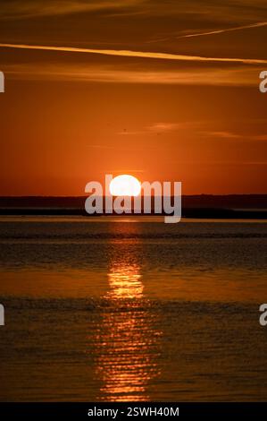 Ein glühender Sonnenuntergang reflektiert sich auf ruhigem Wasser und bildet einen goldenen Pfad Stockfoto