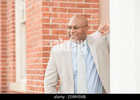Professioneller Mann, der sich an die Wand lehnt und lächelt Stockfoto