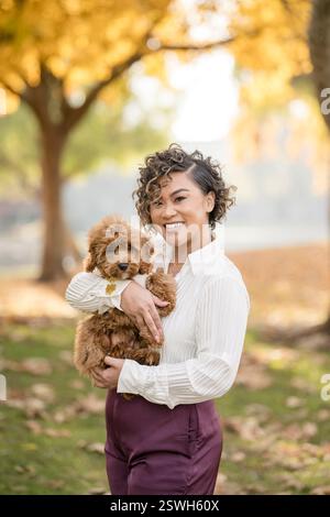 Lächelnde Frau, die ihren flauschigen Hund in einem wunderschönen Herbstpark hält Stockfoto