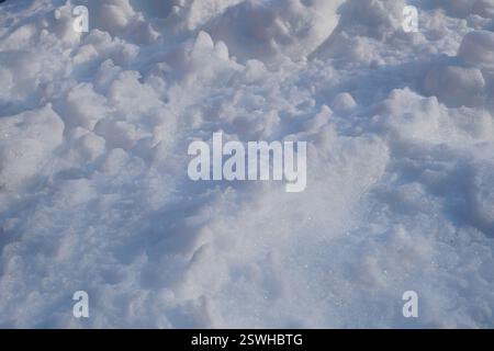Nahaufnahme einer unebenen, strukturierten Schneelage mit zerbröckelten Klumpen und Schatten im Sonnenlicht im Winter Stockfoto