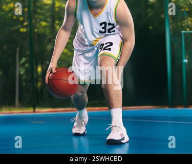 Erwachsene männliche Basketballspieler hüpfen Basketball auf dem Platz im Freien. Muskulöser Basketballspieler mit klassischem Basketball. Basketball-Trainingseinheit für Stockfoto