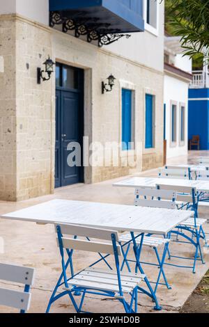 Blau-weiße Tische und Stühle sind ordentlich in einem Essbereich im Freien mit blauen Akzenten und weißen Möbeln angeordnet. Perfekt, um eine Mahlzeit zu genießen Stockfoto