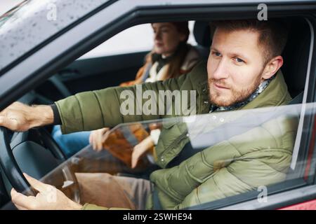Porträt eines Mannes, der auf dem Fahrersitz sitzt und direkt mit fokussiertem Ausdruck auf die Kamera starrt, während sich die Passagiere im Hintergrund befinden Stockfoto