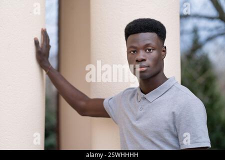 Ein junger Mann mit geschliffenem Kopf und geschliffenem Bart steht vor einer weißen Säule. Er trägt ein graues Hemd und eine graue Mütze Stockfoto