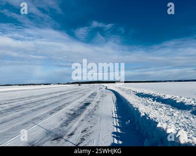 Die Winterlandschaft zeigt eine schneebedeckte Straße auf dem Eis und eine weite Weite unter einem hellen, leuchtend blauen Himmel in Nordschweden. Stockfoto