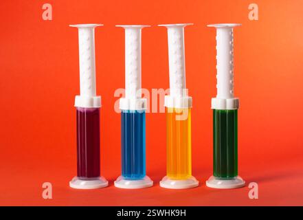 Satz mehrfarbiger Spritzen mit Reinigungsdesinfektionsgel auf rotem Hintergrund, Nahaufnahme Stockfoto