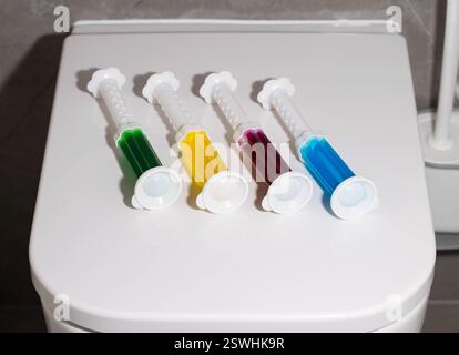Ein Set mehrfarbiger Spritzen mit verschiedenen Düften auf der Toilettenschüssel in der Toilette zur Reinigung und Desinfektion. Hygiene und antibakterielle Wirkung Stockfoto