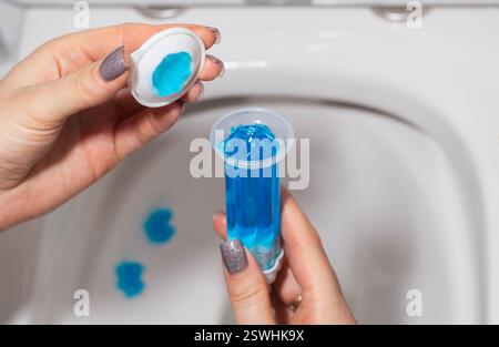 Eine Spritze mit ozeanduftendem Gel zur Reinigung und Desinfektion der Toilette in einer Hand vor dem Hintergrund einer Toilette. Antibakterielle Wirkung Stockfoto