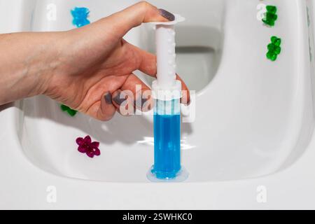 Eine Spritze mit ozeanduftendem Gel zur Reinigung und Desinfektion der Toilette in einer Hand vor dem Hintergrund einer Toilette. Antibakterielle Wirkung Stockfoto
