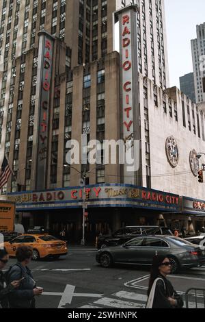 New York, USA - 8. April 2024: Eine lebendige Straßenszene in der Radio City Music Hall. Der legendäre Art déco-Veranstaltungsort, Neonlichter, Taxis und Fußgänger fangen ein Stockfoto