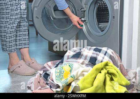 Frau im Schlafanzug steckt Waschmittelkapsel in eine offene Waschmaschine. Reinigung und Ordnung in der Wohnung. Moderne Einrichtung und Lifestyle. Stockfoto