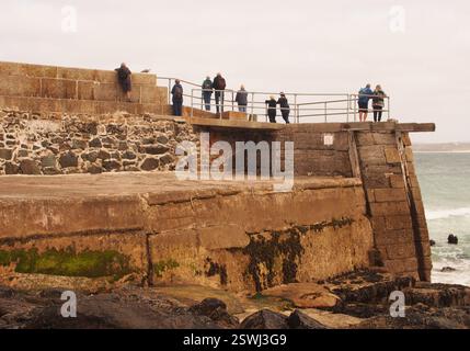Urlauber stehen am Ende des New Pier St Ives, Cornwall, England, Großbritannien, mit Blick auf das Meer und die Wellen auf dem Meer Stockfoto