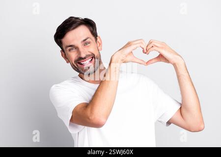 Lächelnder junger bärtiger Mann, der Herzform macht, mit Händen, die in lässigem Stil vor einem hellgrauen Hintergrund gekleidet sind Stockfoto