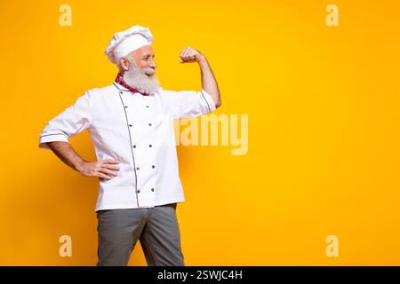 Chefkoch in Uniform, der seinen Arm selbstbewusst vor einem leuchtend gelben Hintergrund biegt Stockfoto