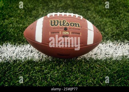 Nahaufnahme eines American Football Balls der Marke Wilson, der auf dem grasbewachsenen grünen Sportfeld mit weißer Linie liegt Stockfoto