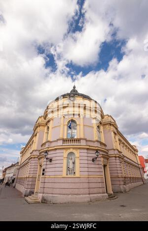 Majestätische architektonische Struktur mit gelben und rosafarbenen Details, neoklassizistischem Stil und Skulpturen, unter einem dynamischen Himmel, der von Fl dominiert wird Stockfoto
