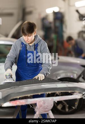Junger Mann Automechaniker poliert Karosserieteile mit Autopufferpolierer Werkzeugmaschine Stockfoto